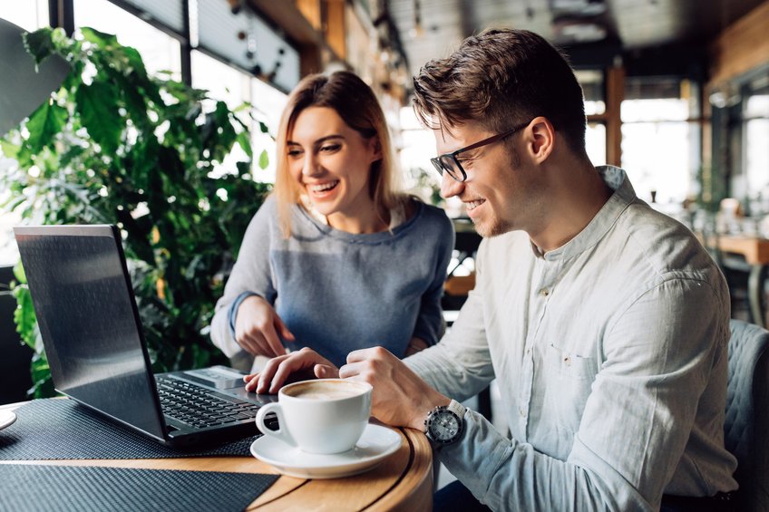 A woman and a man are sitting in front of a laptop with a cup of coffee.