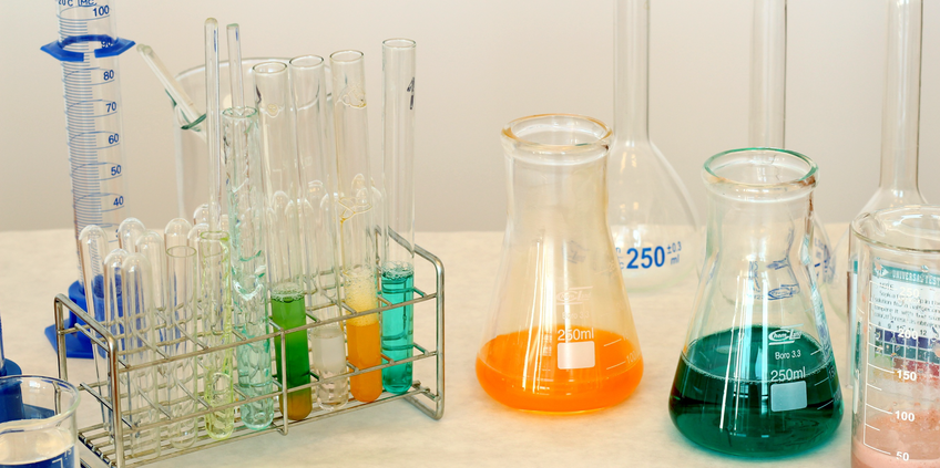 Find chemical data, properties and compounds! View on a table in a laboratory with test glasses filled with liquids in green, yellow and turquois as well as other glass container filled with liquids in yellow and green.