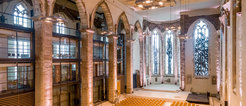Interior of St. John's church in Magdeburg, with preserved stone arches, modern glass elements, and a spacious seating area facing a stage.
